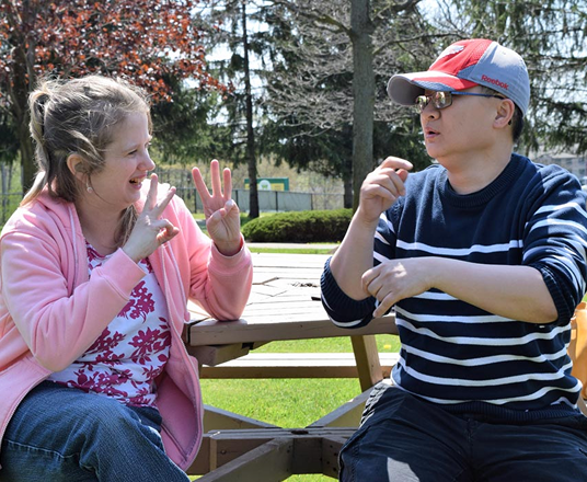 Two people sitting outdoors and communicating in sign language